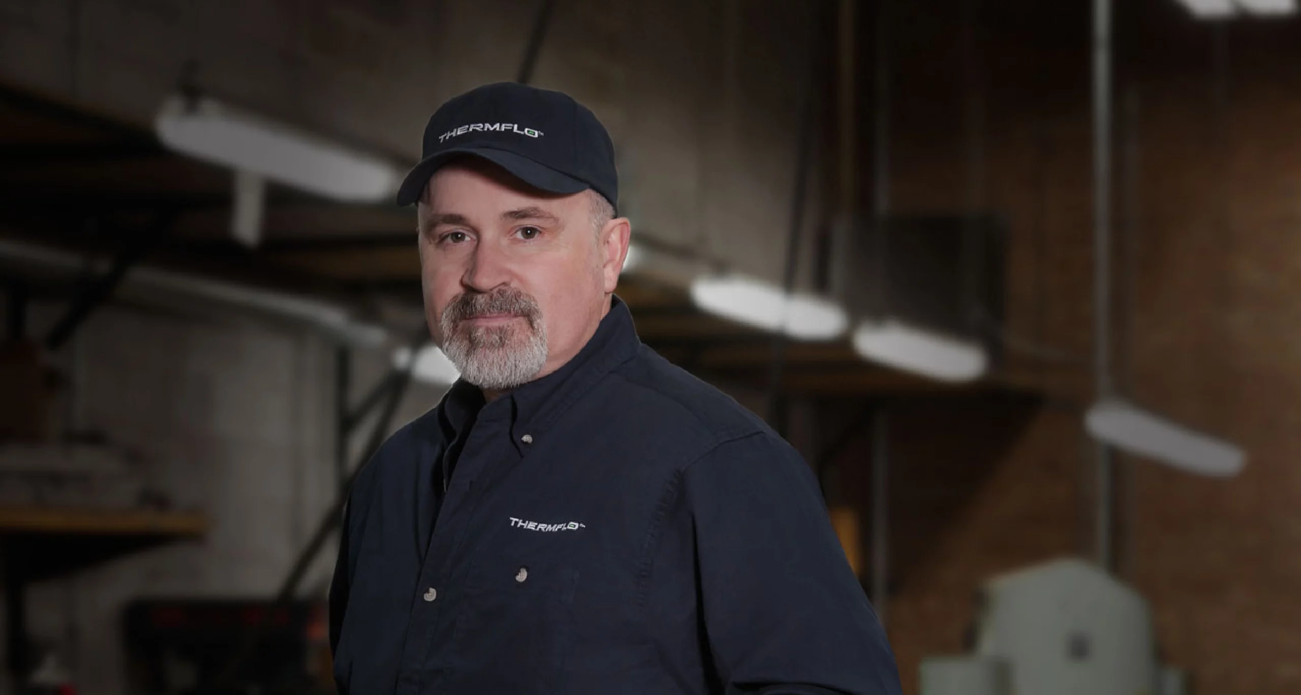 Thermal employee wearing uniform with embroidered logos on baseball cap and button up work shirt.